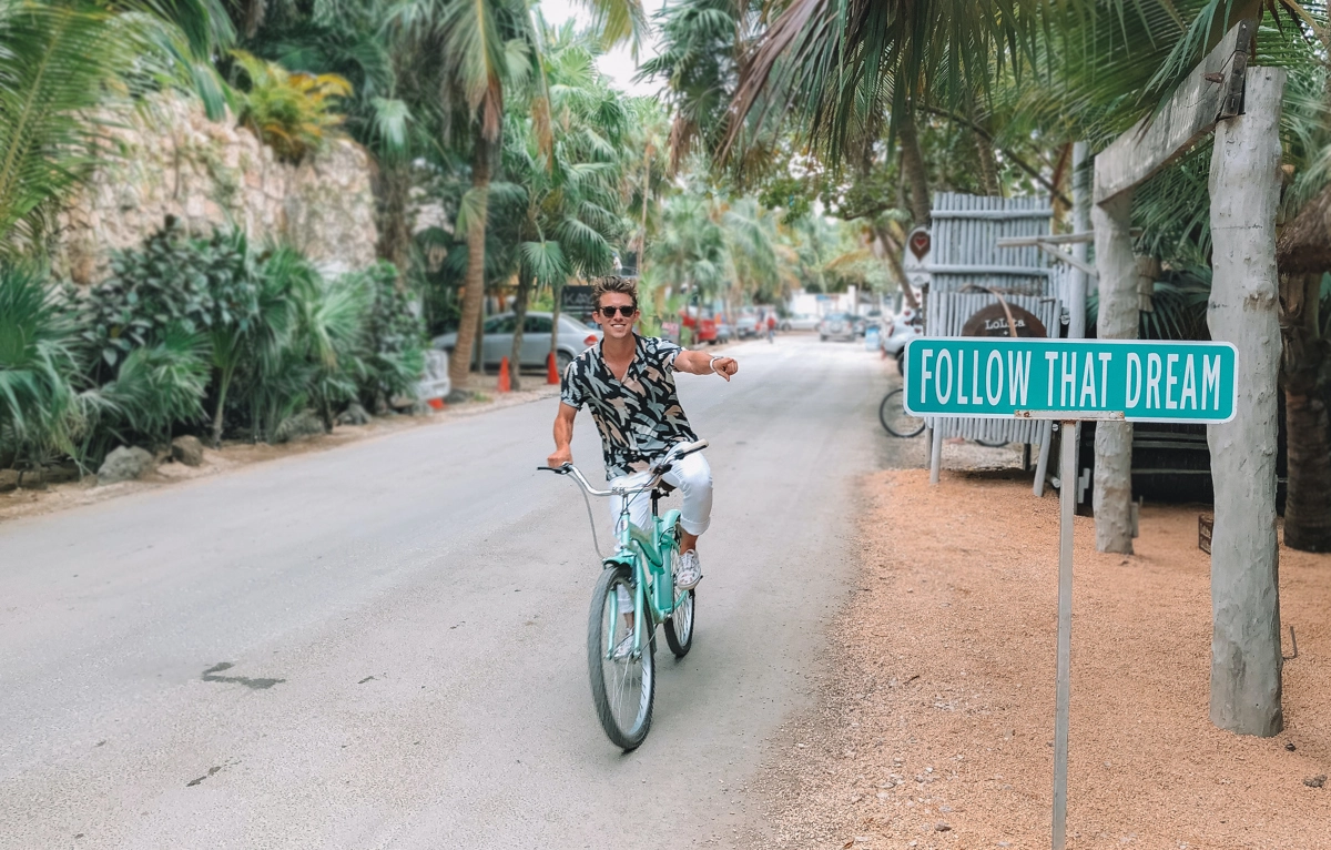 Man riding a bicycle pointing at a sign with "follow your dream"